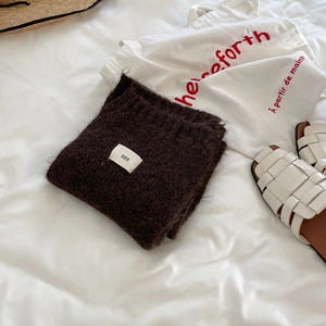 Detail of dark brown wool scarf folded on white bedding with a stylish canvas tote bag