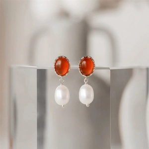 Macro shot of silver drop earrings featuring orange gemstones and white freshwater pearls