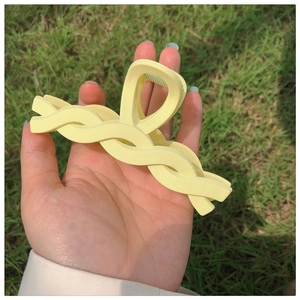 Close-up of a matte yellow twisted shark hair claw clip held outdoors over green grass