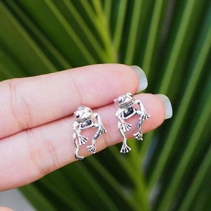 Detailed view of vintage silver frog stud earrings held against a leaf background
