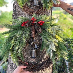 Handcrafted Christmas wreath with pine needles, red berries, and bells hanging on tree