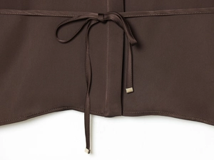 Detail of a brown poplin shirt featuring a back tie knot with gold metal tips