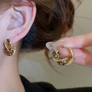 Detailed close-up of gold-plated hoop earrings with tiger eye beads and woven texture