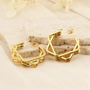 Close-up of gold layered hexagonal earrings on a textured stone tray with white flowers