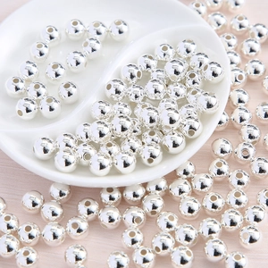 Detailed view of glossy silver round beads for DIY jewelry making on a white tray