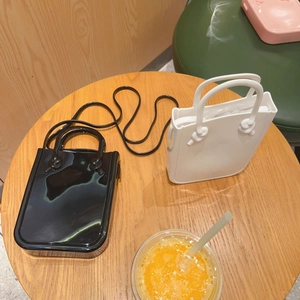 Mini PVC jelly handbag and white matte tote displayed on a wooden table in a cafe setting