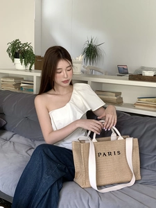 Straw tote bag with long white shoulder straps and black Paris text for beach vacations