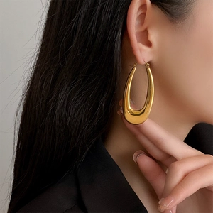 Macro shot of large polished gold U-shaped oval hoop earrings on model ear