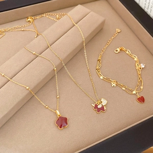 Detail view of gold-plated jewelry set with red clover pendants and pearl accents in a box