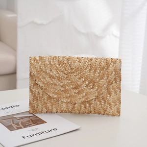 Minimalist straw woven clutch bag with semi-circular flap shown on a clean white desk