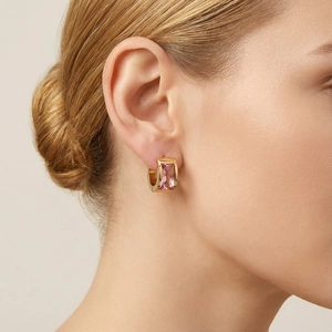 Detailed close-up of golden hoop earrings featuring a baguette-cut pink gemstone on a model