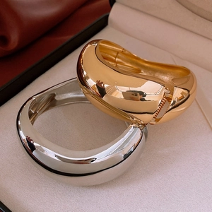 Macro shot of minimalist gold and silver wide bangles with polished mirror finish