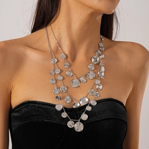 Detail of layered silver necklaces featuring textured circular metal charms and chains