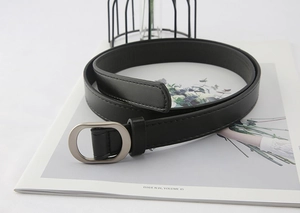 Detail of a black faux leather belt with a silver oval buckle on a fashion magazine