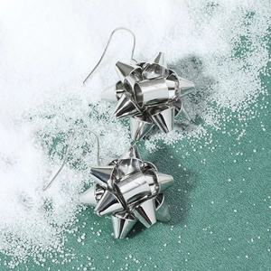 Detail of silver ribbon flower earrings with polished finish against festive green backdrop