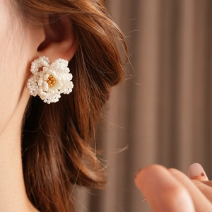 Close-up of elegant white beaded camellia flower earring worn by a model in soft lighting