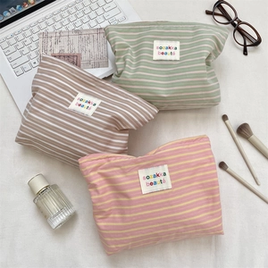 Flat lay of three striped cosmetic bags in pink, green, and brown with a canvas texture