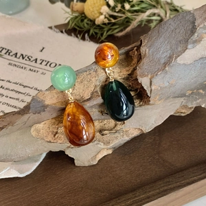 Detail view of asymmetrical resin teardrop earrings on a rustic wood branch
