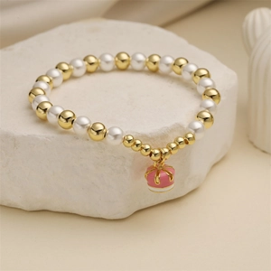 Beaded bracelet with white pearls, gold copper beads and pink crown enamel charm on stone
