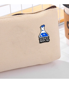 Close-up of Science Addicted blue beaker enamel pin pinned to a beige canvas bag
