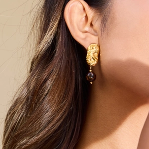 Détail de boucle d'oreille vintage dorée avec perle marron foncée portée par un modèle
