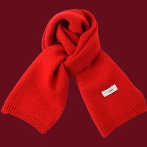 Close-up of a soft red knitted winter scarf with a white brand label and elegant knot detail