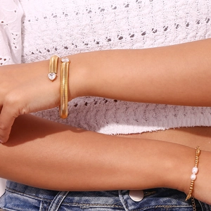 Detail of 18K gold heart zircon bangle and pearl bead bracelet on woman's wrist