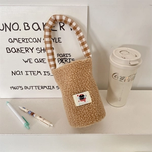 Detalle de bolsa de peluche marrón para botella con asa de cuadros y parche de gato