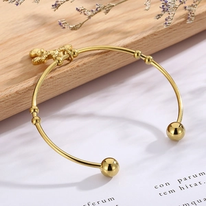 Detailed view of a gold rose cross open bangle with a polished finish on a wooden tray