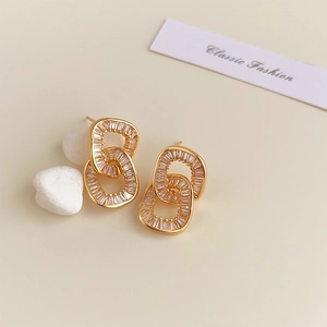 Detailed macro view of 18K gold intertwined hoop earrings with zircon stones on pebble