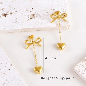 Golden bow earrings with heart tassel pendants and size specifications on stone background