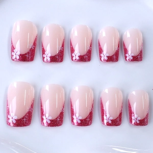 Pink French press-on nails with red glitter tips and white flower designs on white background