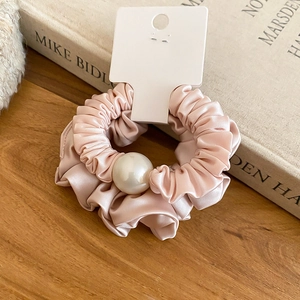 Détail macro du chouchou en satin rose poudré élégant avec grande perle blanche sur un livre