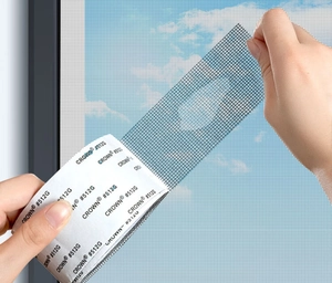 Close-up of hand peeling adhesive backing of grey screen repair tape against blue sky