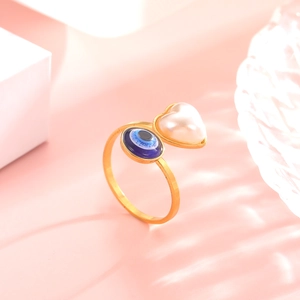 Adjustable golden evil eye ring with blue bead and heart pearl on a stylish background