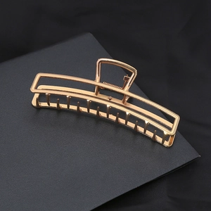 Minimalist rectangular hollow gold metal hair claw clip on dark textured surface