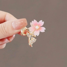 Detail of a golden cherry blossom hair clip with pink enamel and a central pearl accent