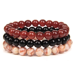 Detailed close-up of three stacked 8mm natural stone bead bracelets in red, black, and white