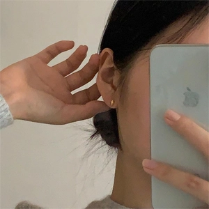 Minimalist small golden oval stud earrings shown worn in a casual lifestyle selfie view