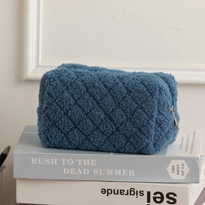 Detail of navy blue fuzzy pouch with diamond quilted texture and smooth metal zipper