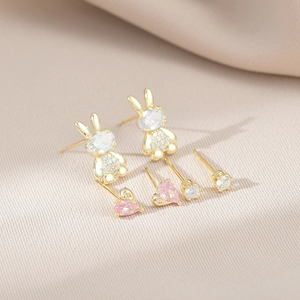 Three pairs of elegant gold rabbit, pink heart and crystal stud earrings on silk fabric