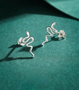 Detailed macro view of minimalist S925 sterling silver snake earrings on green background