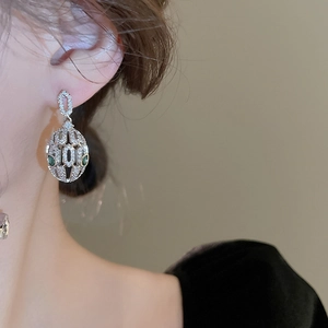 Close-up of silver oval hoop earrings with clear pavé stones and green gemstones