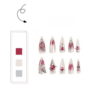 Gros plan d'ongles stiletto à coller avec dégradé bordeaux, breloques argentées et papillon 3D