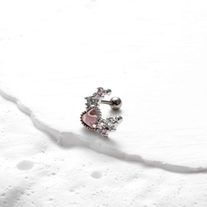 Macro shot of pink heart gemstone barbell earring on a textured white stone background