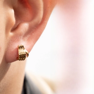 Gros plan d'un clou d'oreille doré en forme de main évidée avec détails sculptés