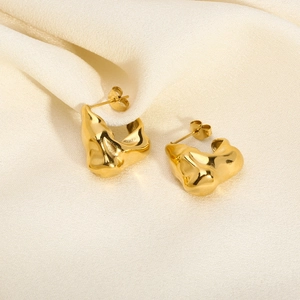 Macro shot of irregular pleated V-shaped gold earrings on soft beige silk fabric