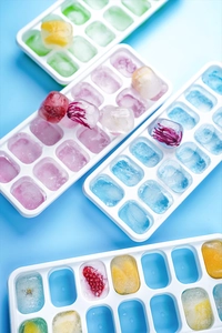 Top view of four colorful 14-grid ice cube trays with frozen fruits and flowers inside