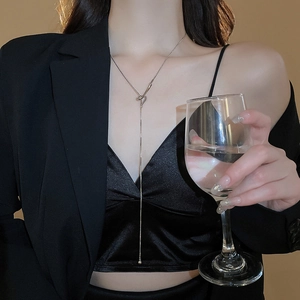 Close-up of a silver knot pendant necklace with dangling metal beads worn on a model