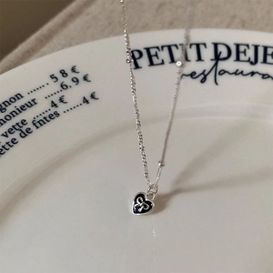 S925 silver necklace with black heart pendant and bow detail on a white ceramic plate